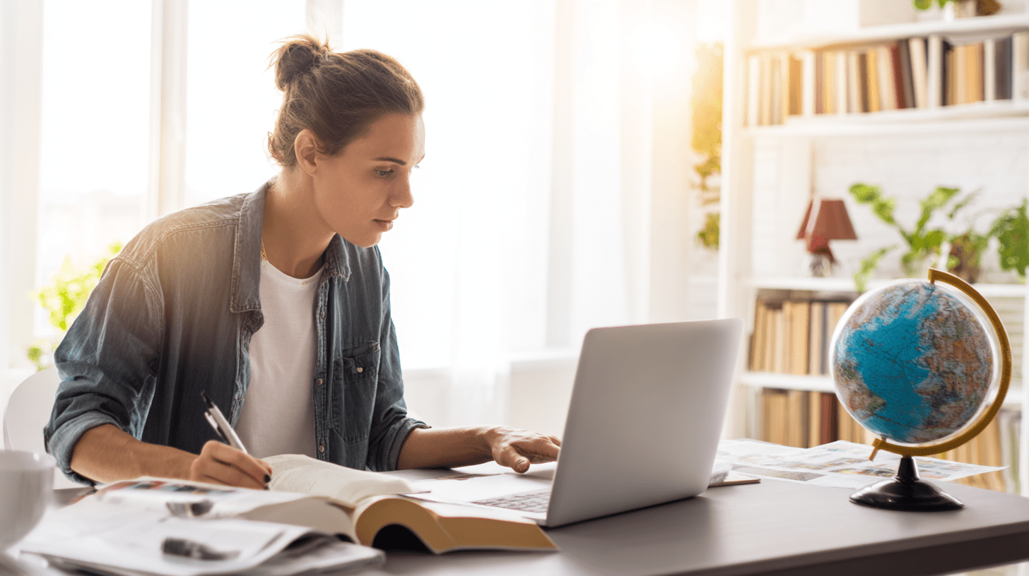Uczeń planujący studia za granicą przy biurku z laptopem, globusem i informatorami uczelni zagranicznych