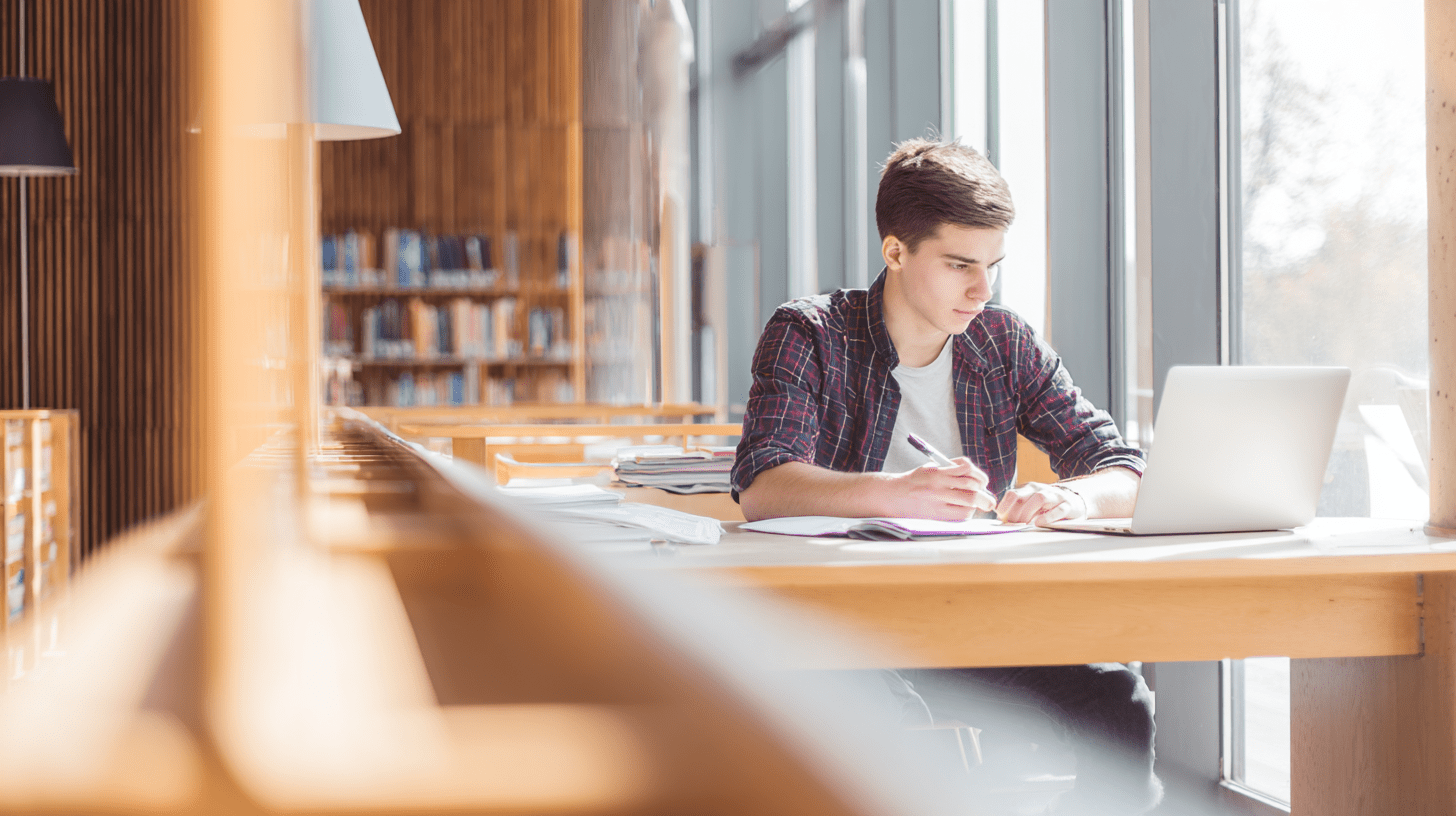 Młody student przeglądający ofertę edukacyjną i kierunki na Politechnice Wrocławskiej na laptopie w nowoczesnej bibliotece.