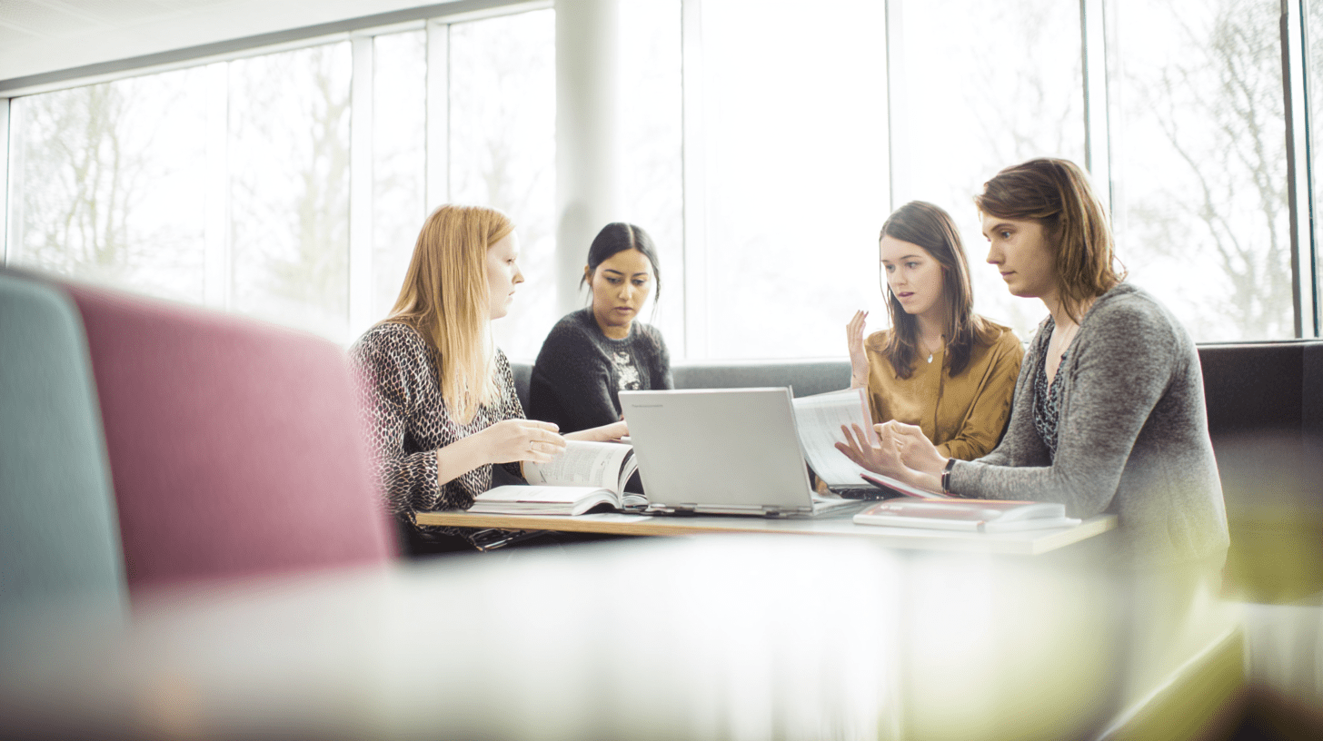 Grupa studentów kierunku psychologia biznesu wspólnie omawia projekt przy laptopie w nowoczesnej bibliotece.